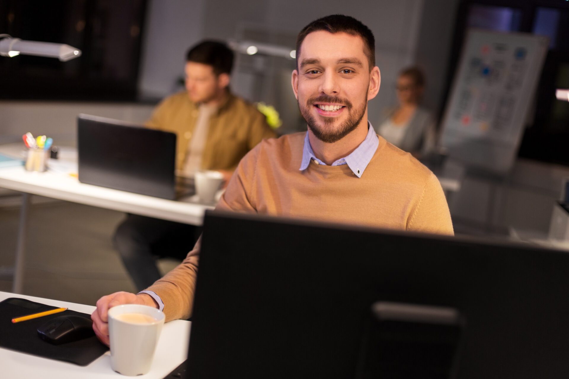 technician smiling with a mug work on a computer